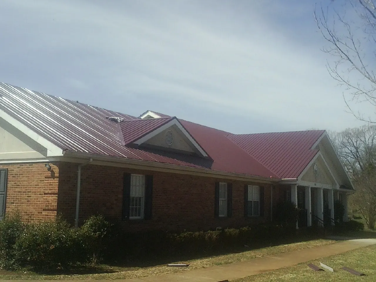 Red metal roof with gabled entries on a long brick building, from a Hail Damage Roof Repair job in Mississippi State
