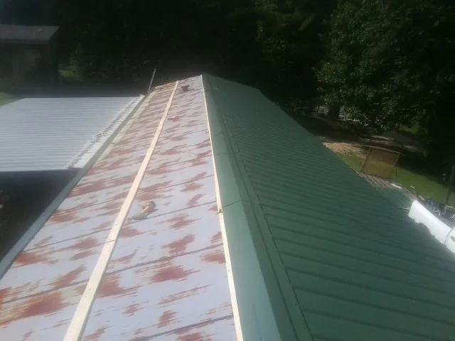 Old rusted panels beside newly installed green metal roofing — Wind Damage Roof Repair by Roofing Brothers in Mississippi State