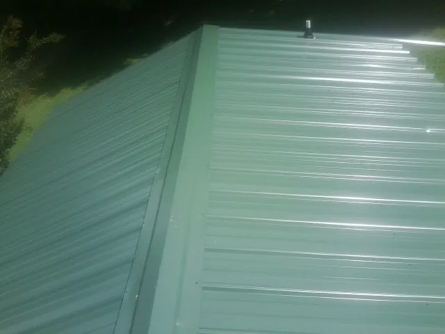 New green metal panels meeting at the ridge of a roof — Flat Roof Repair work by our crew in Mississippi State