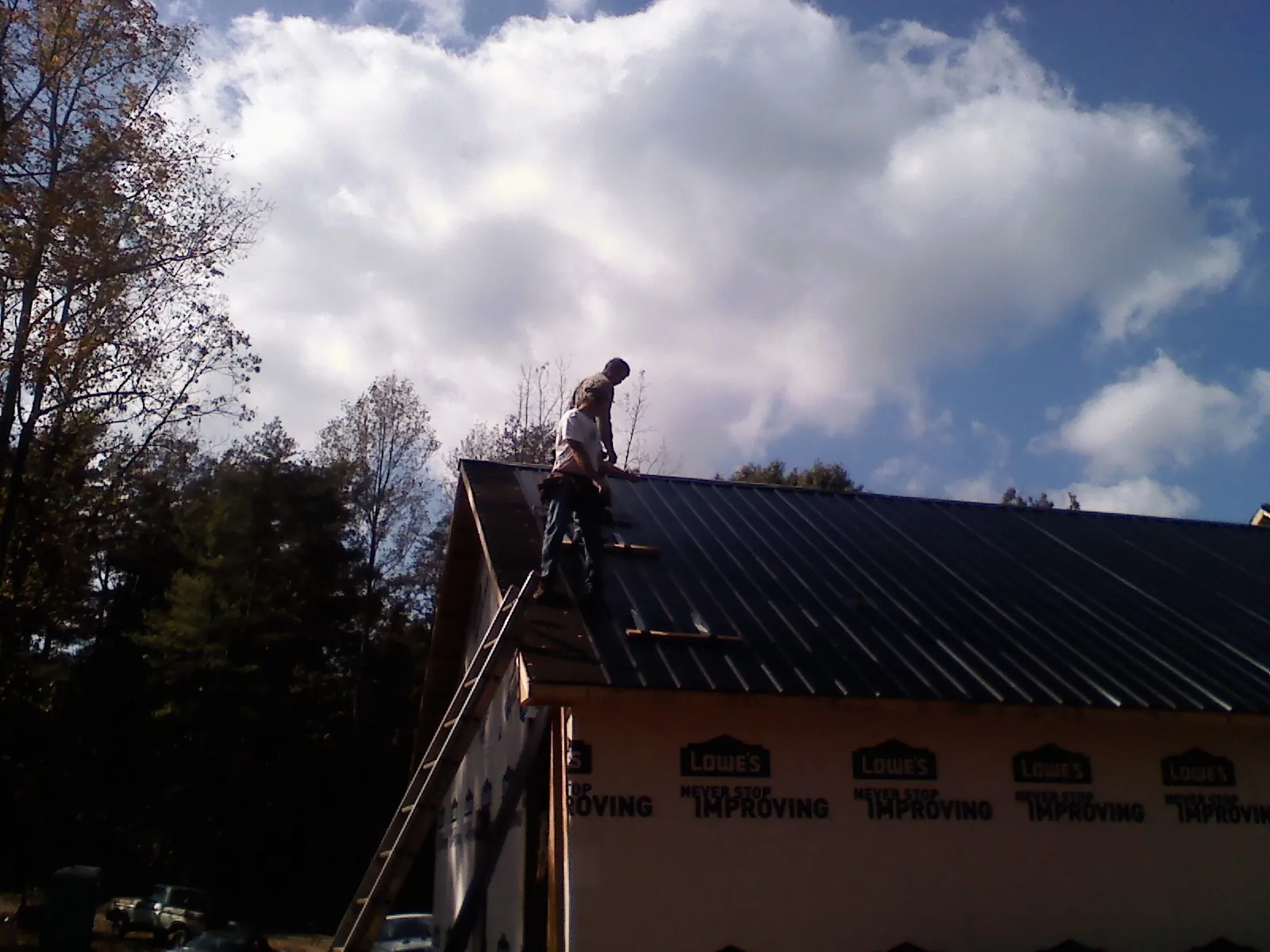 Roofer fastening dark metal panels high against a cloudy sky, from a Roof Inspection job in Mississippi State