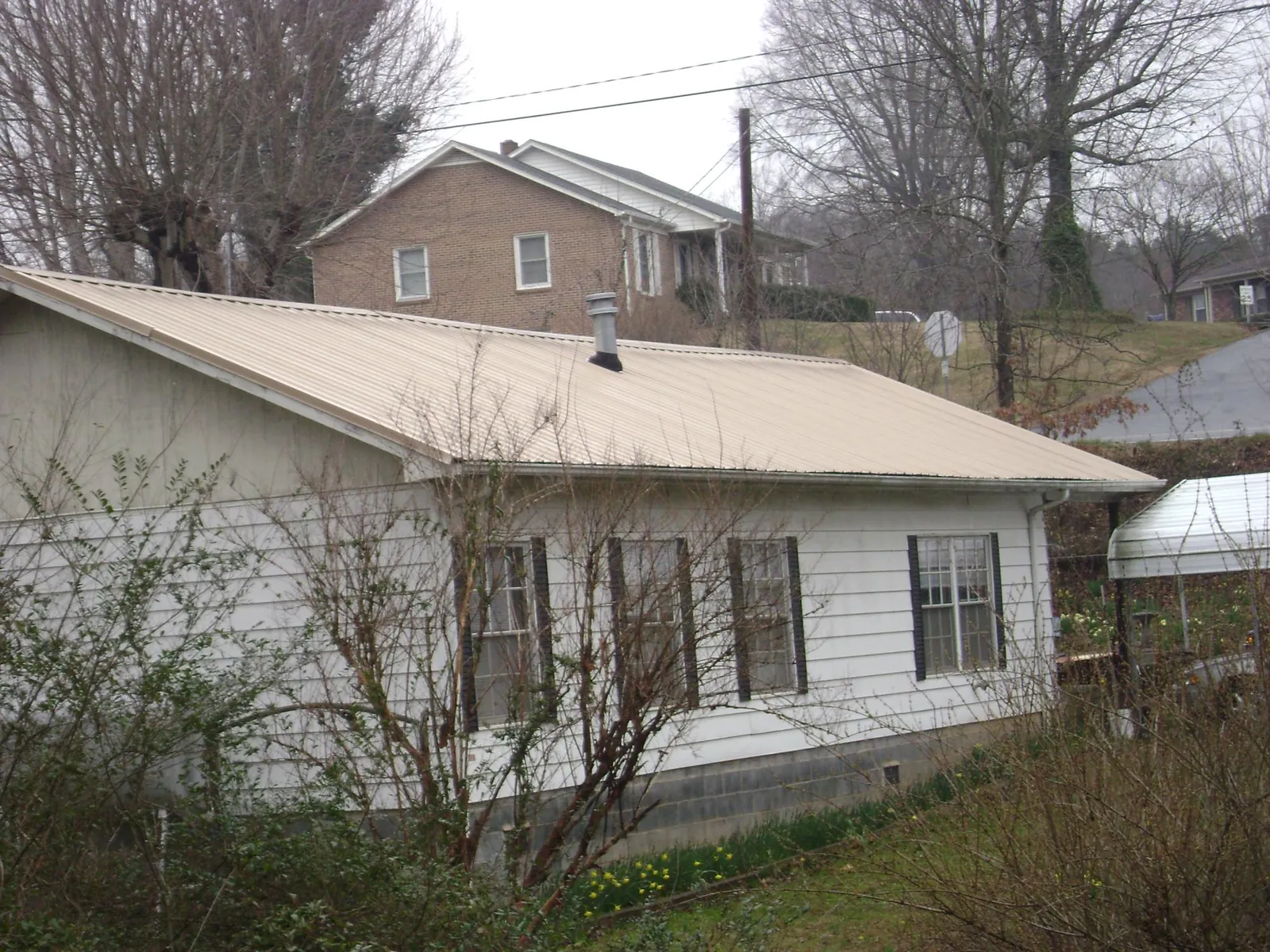 Tan metal roof on a white sided house set into a hillside — Commercial Roofing by Roofing Brothers in Mississippi State