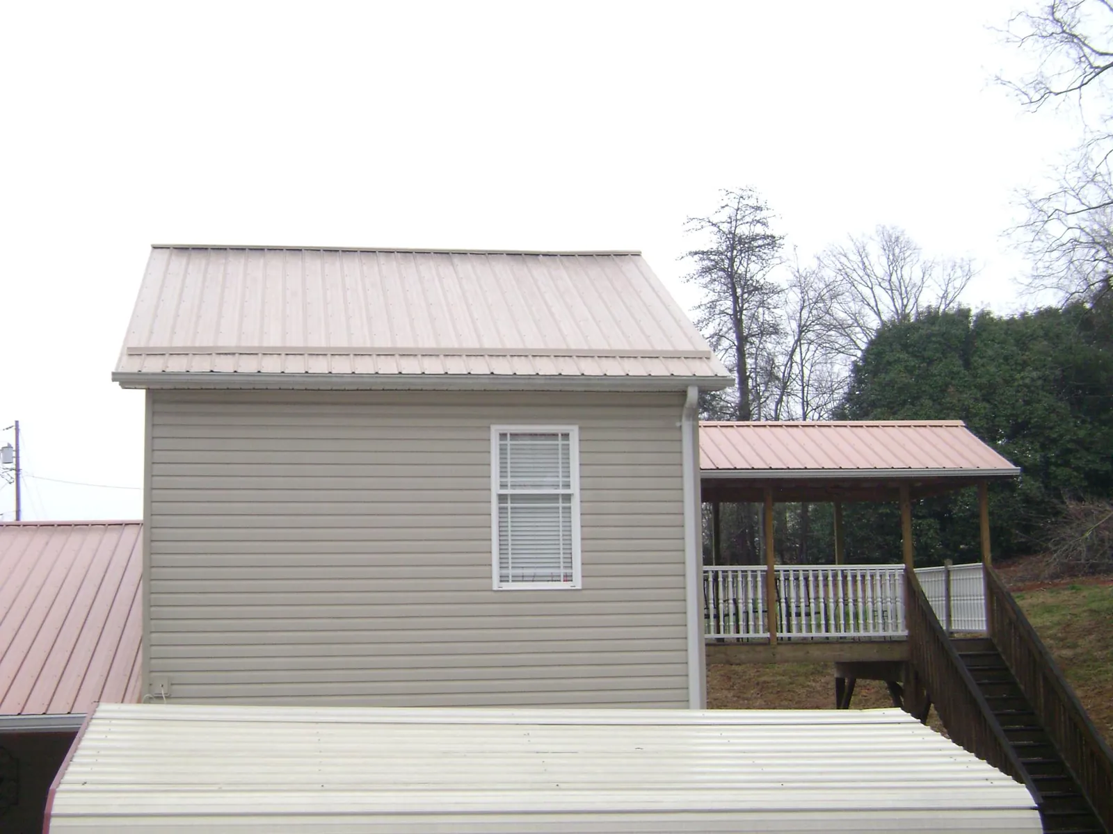 Tan metal roofs on a two story addition and attached porch, from a Roof Replacement job in Mississippi State